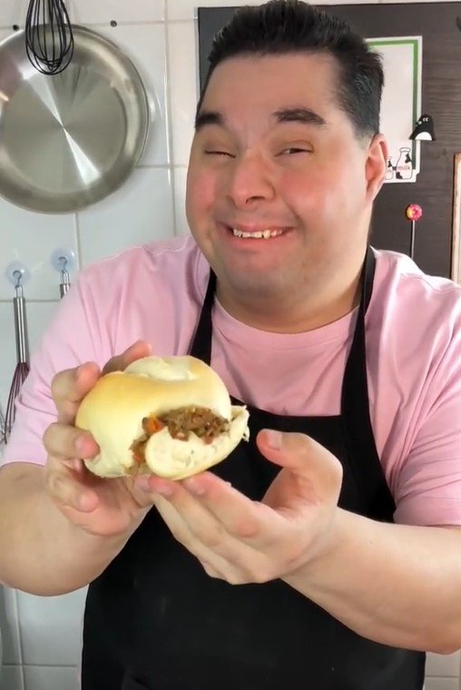 Na foto, um homem segura um sanduíche de pão francês com carne
