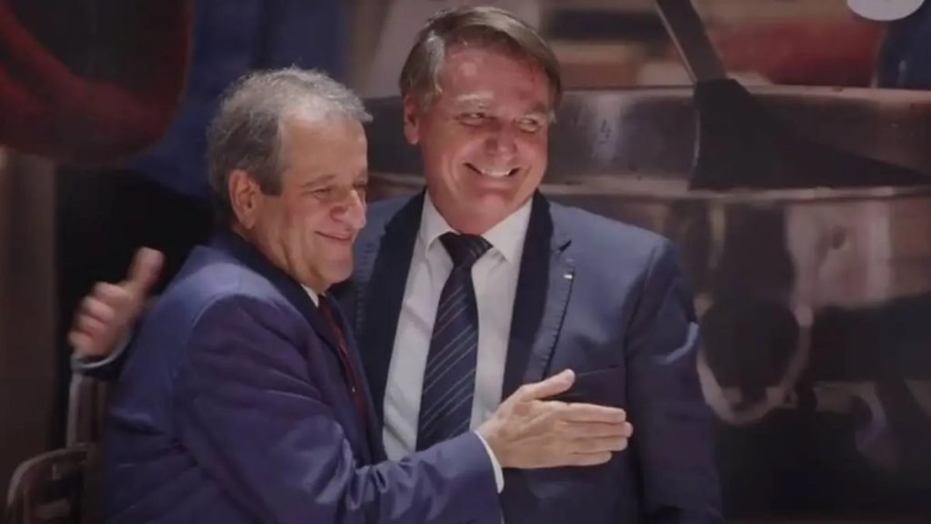 Fotografia colorida. Valdemar (esquerda) e Bolsonaro (direita) se abraçam e sorriem na filiação de Jair ao PL