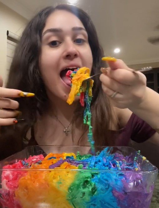 Na foto, uma jovem come um macarrão colorido