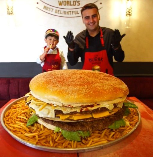 Na foto, um homem posa em frente a um hambúrguer gigante com uma criança do lado
