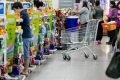 Em um ambiente de supermercado, pessoas na fila separadas por gôndolas. Ao fundo um carrinho de mercado vazio.