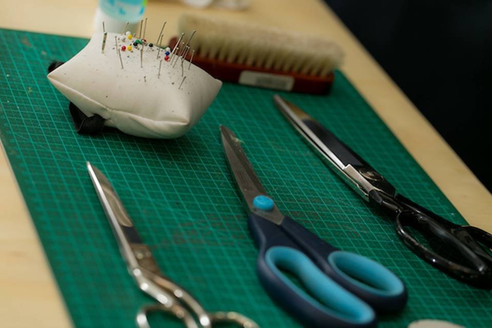 Uma mesa com vários elementos de costura em cima. Tesouras de tipos diferentes, uma almofada com agulhas e uma escovinha de limpar pelo da roupa