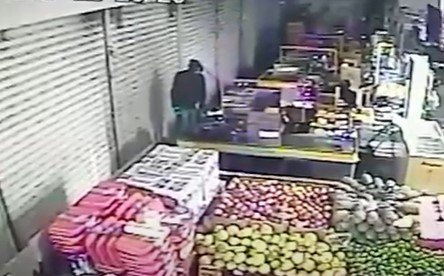 Homem de casaco e capuz preto no meio de um mercado, em área, ao que parece, de feira
