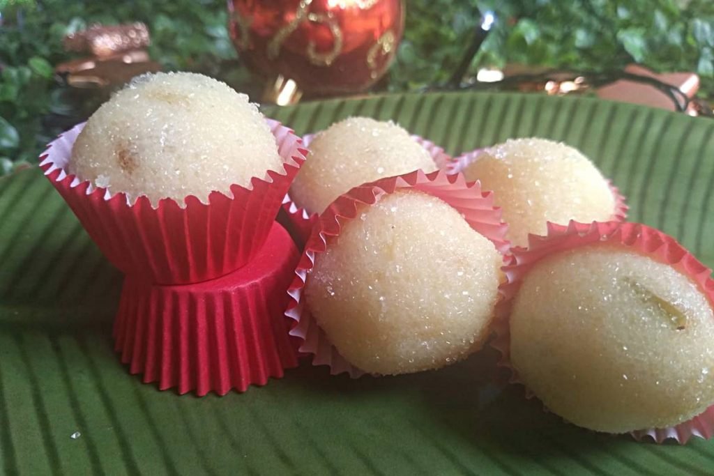 Na foto temos uma bandeja verde com cinco brigadeiros brancos em cima e ao fundo decoração de natal