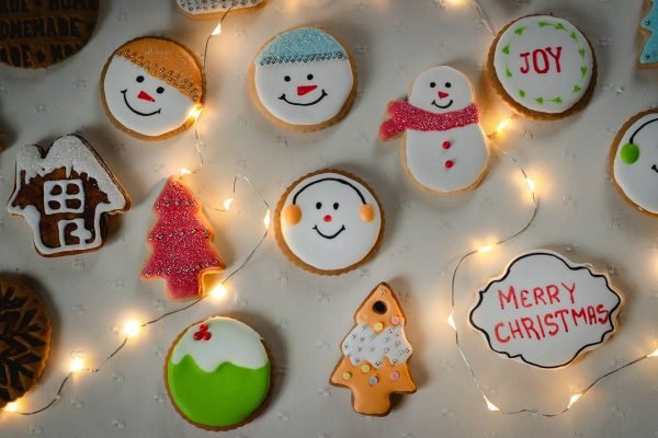 Na foto temos biscoitos redondos com rostos desenhados, biscoitos em formato de arvore de natal e outros em formato de boneco de neve