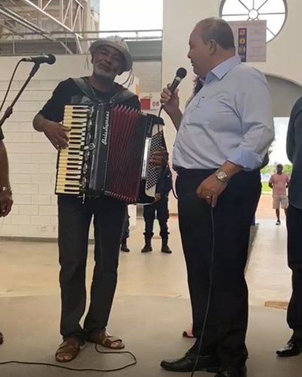 Homem segura sanfona ao lado de homem com microfone