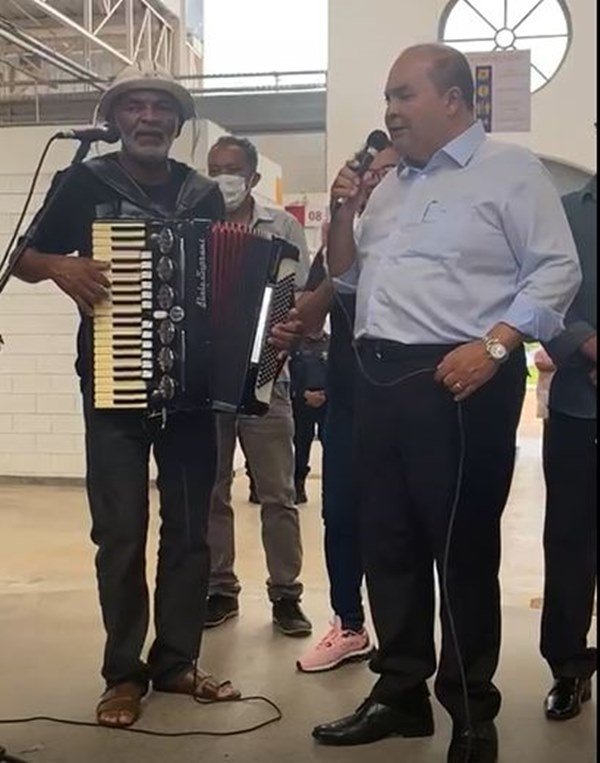Homem segura sanfona ao lado de homem com microfone