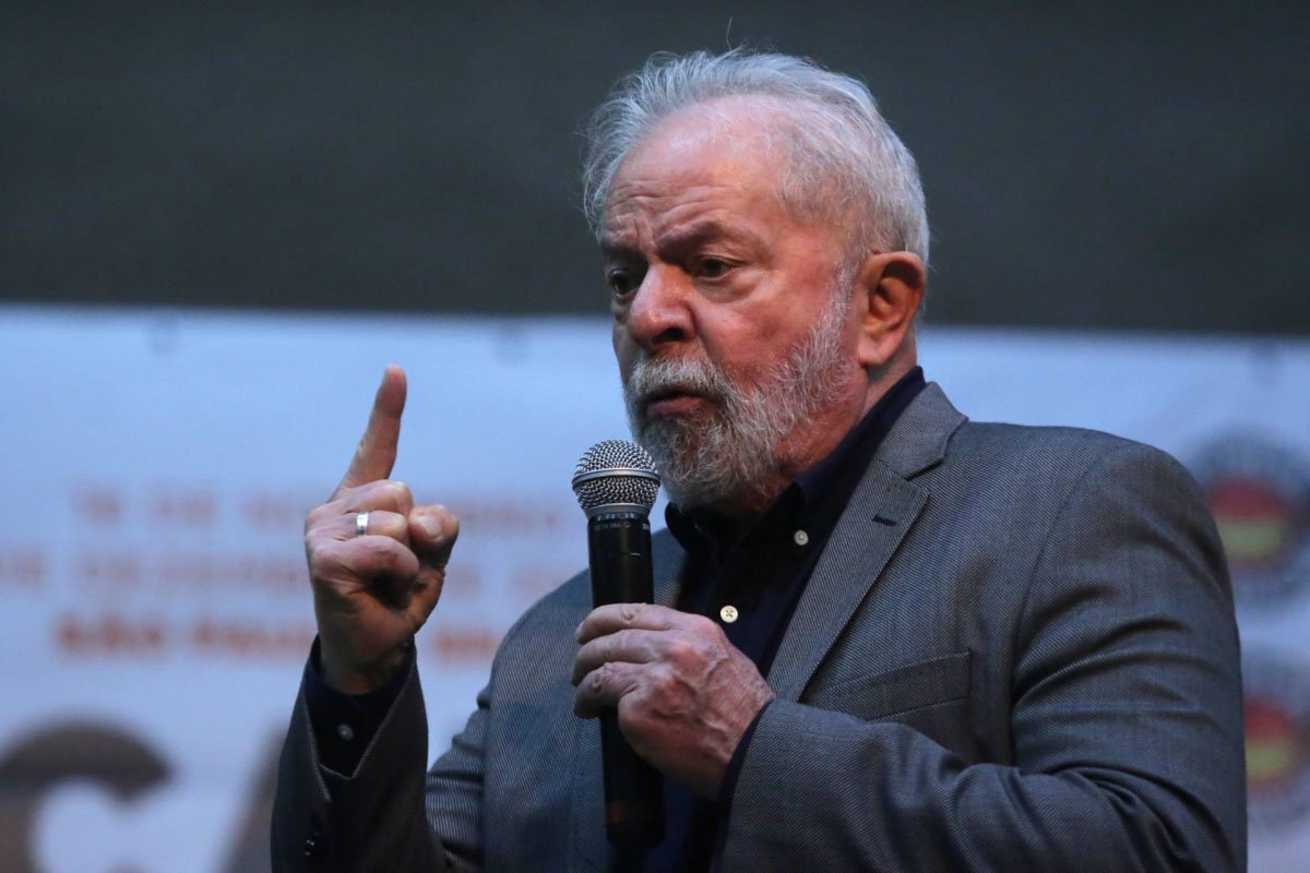 Ex-presidente Lula (PT) fala ao público. Ele está de lado e usa terno, olhando para frente. Segura um microfone e gesticula, sério, sob um fundo cinza - Metrópoles