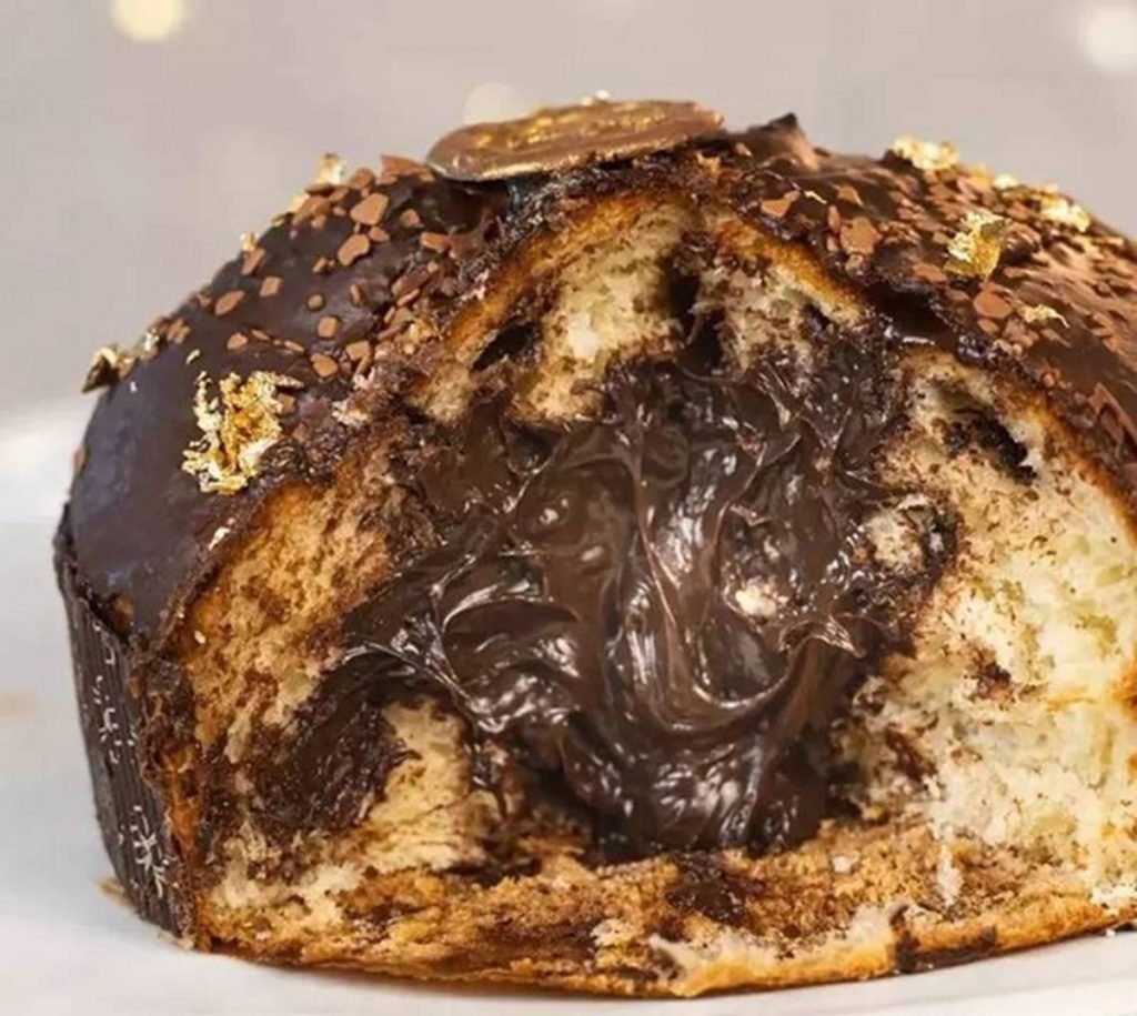 Na foto temos um chocotone baixo, como uma colomba pascal, que tem massa branca e recheio marrom escuro, de chocolate