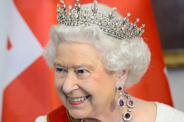 In the color photograph, Queen Elizabeth is smiling in the middle of the picture and wearing the royal crown.