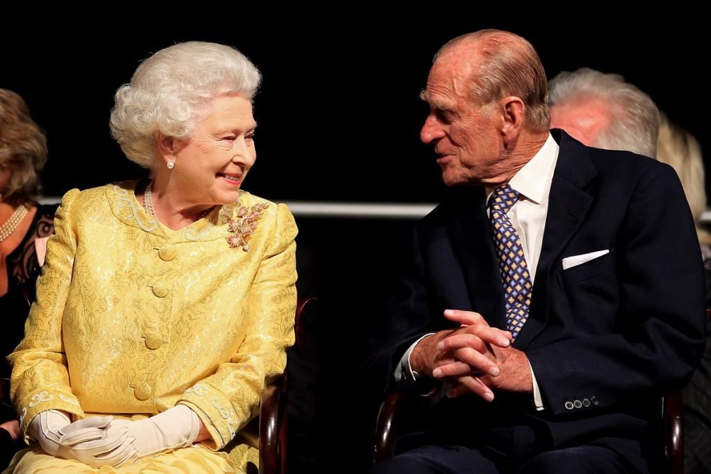 Na fotografia colorida, Elizabeth II aparece à esquerda sorrindo para o ex-marido príncipe Philipe (à direita) da imagem de terno
