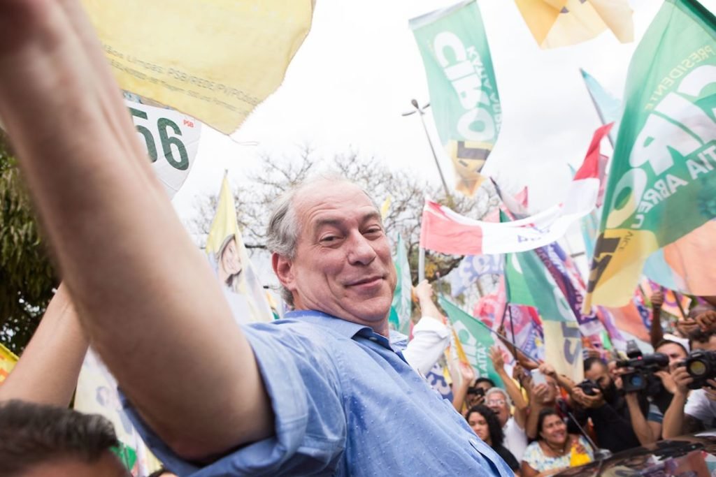 Fotografía en color de Ciro Gomes.  Es un hombre blanco con cabello gris liso en el costado.  Se le representa con los brazos abiertos en medio de una multitud.