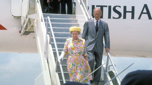 Fotografia colorida. Rainha Elizabeth II e o príncipe Philip aparecem desembarcando de avião