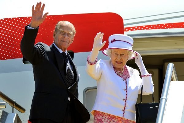 Na fotografia colorida, a rainha Elizabeth II e o príncipe Philip aparecem acenando para o público que o aguarda no desembarque do voo