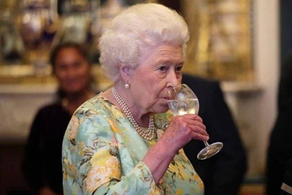 Na fotografia colorida, a rainha Elizabeth II aparece bebendo um líquido em uma taça
