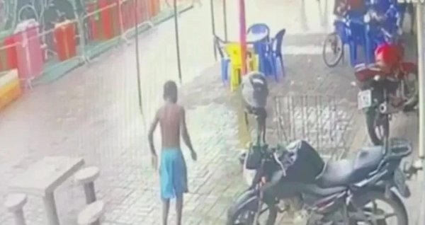Na imagem colorida da câmera de segurança, um menino de bermuda azul aparece de costas em bar