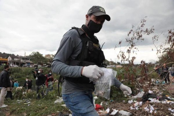Na fotografia colorida, um agente da polícia aparece segurando saco plástico com informações sobre restos mortais encontrados no local