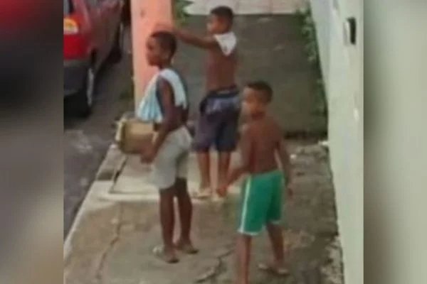 Na imagem colorida de câmera, as três crianças aparecem de costas andando em rua de bairro vizinho