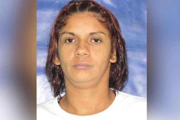 Na fotografia colorida, a traficante aparece séria em foto. Ela veste camiseta branca