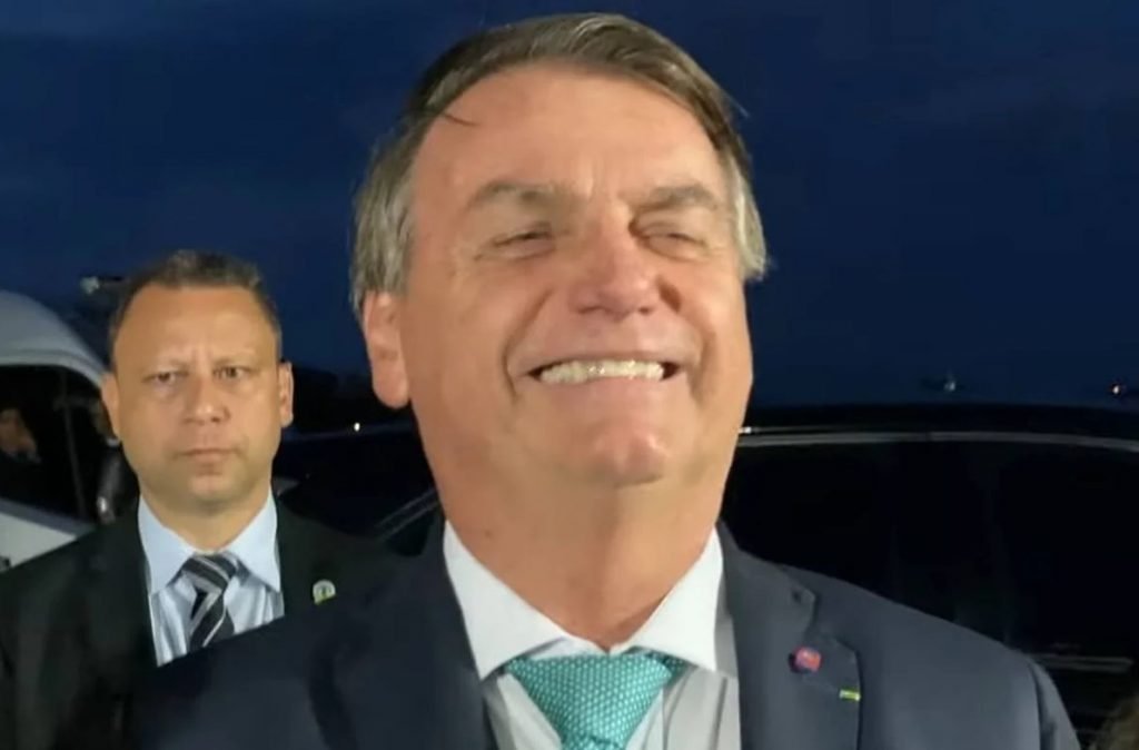 Na imagem colorida, um homem está centralizado. Ele usa terno escuro e camisa branca