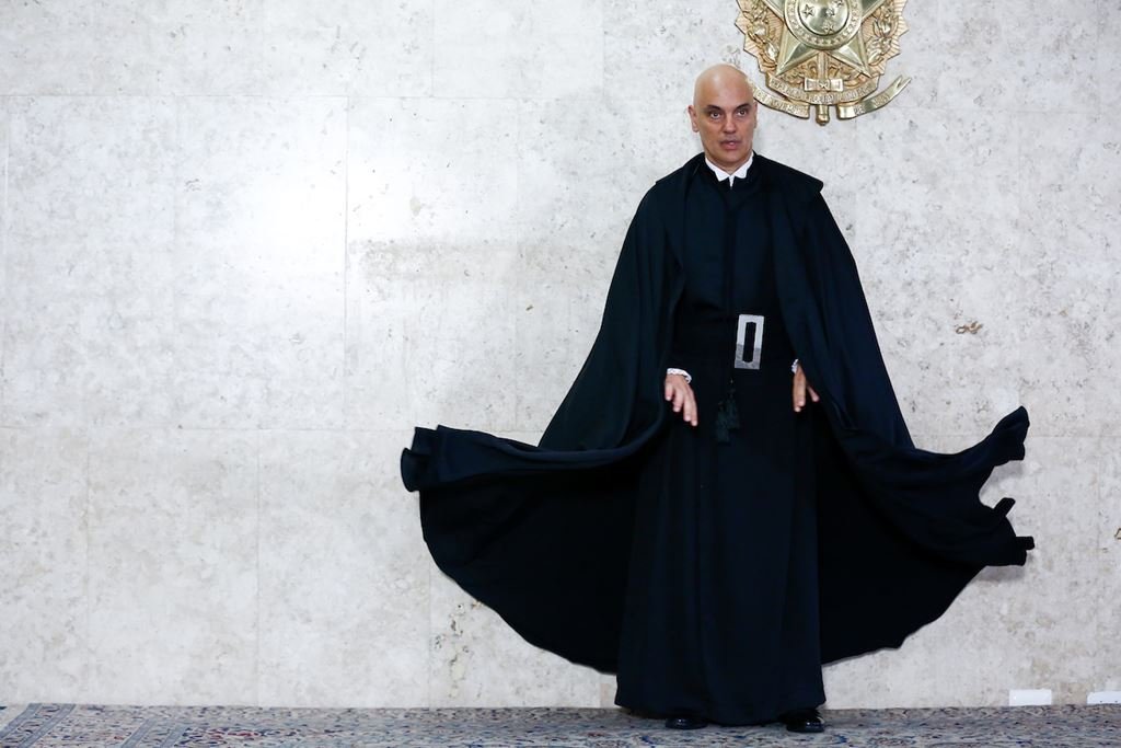 Na imagem colorida, um homem está centralizado. Ele usa terno escuro e camisa branca