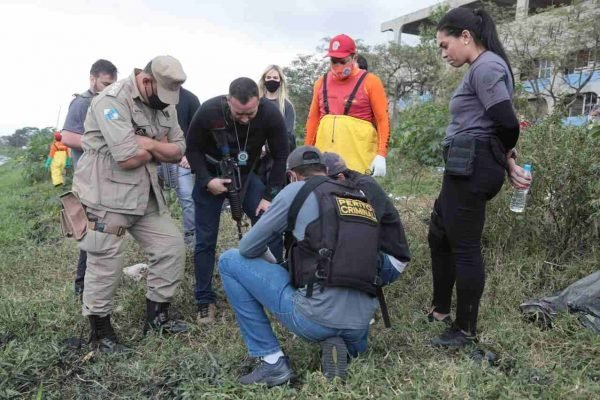 Na ftoografia colorida, agentes policiais coletam informações sobre os restos mortais das crianças desaparecidas