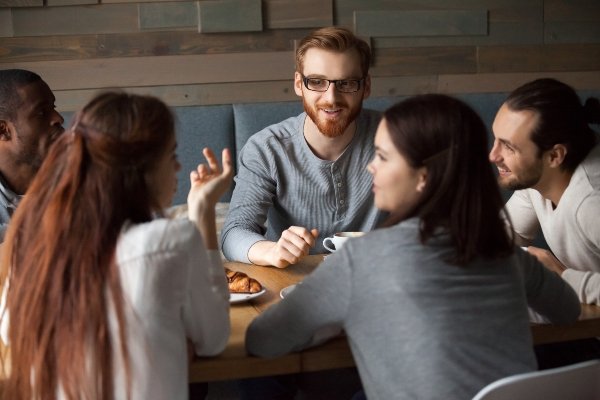 Farbbild von fünf Personen, die an einem Tisch sitzen und sich unterhalten