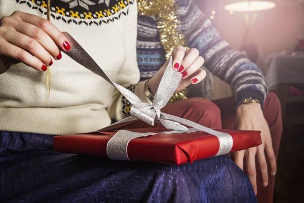 Mão com unhas vermelhas abrindo presente de Natal
