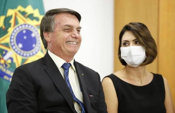 In the colorful photo, Michelle is seen sitting next to her husband wearing a mask.  Bolsonaro sits and smiles at the audience
