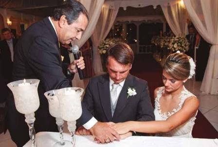 Na fotografia colorida, Michelle e Jair aparecem ajoelhados com as mãos na cerimônia de casamento realizado pelo Silas