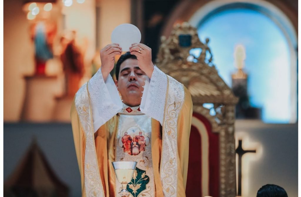 Na fotografia colorida, padre Robson aparece no rito de comunhão durante missa