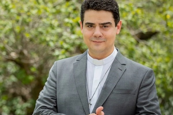 Na fotografia colorida, padre Robson posa para foto de terno e mãos juntas