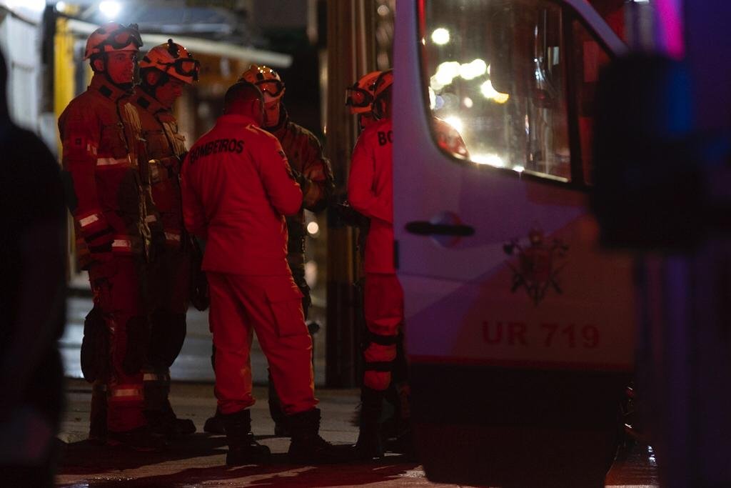 Bombeiros de laranja conversando em uma roda e próximos a um carro