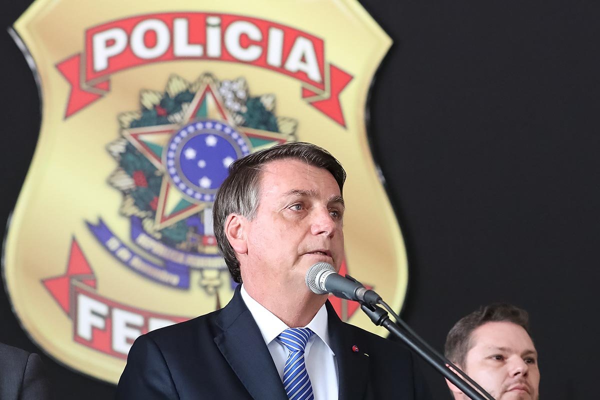 Foto colorida. Bolsonaro com a logo da Policia Federal ao fundo
