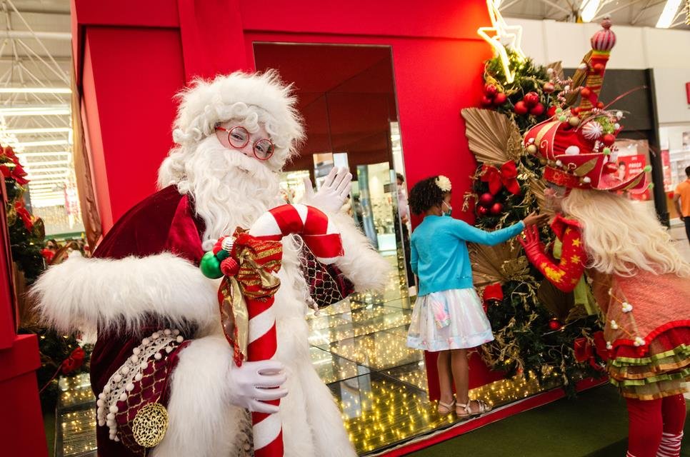 Papai Noel segurando presente e criança ao fundo