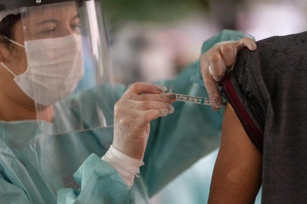 Fotografia colorida. Enfermeira aplica dose de vacina no braço de pessoa
