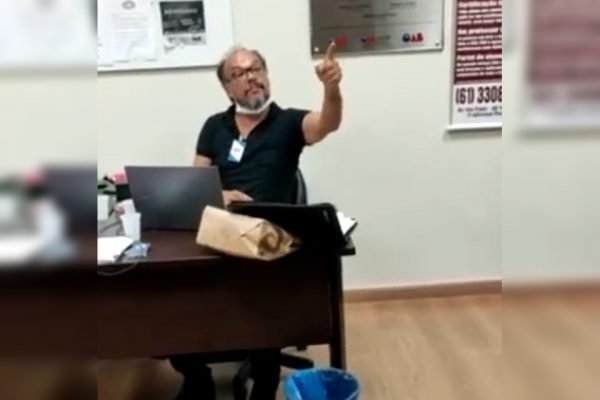 Homem sentado em mesa de madeira e apontando com o dedo para frente