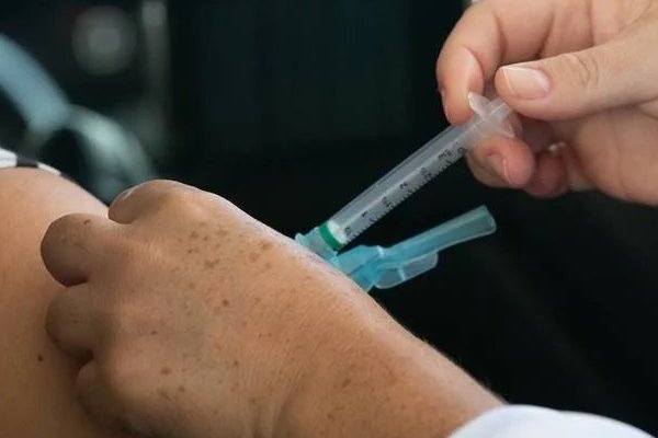 fotografia colorida.  Enfermeira aplica vacina no braço de pessoa