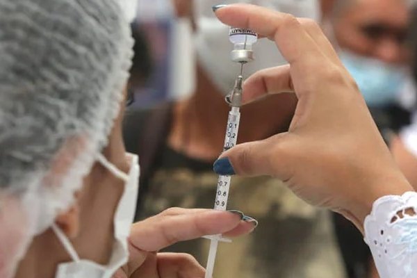 fotografia colorida.  A enfermeira dosa a quantidade de vacina em uma seringa para uso