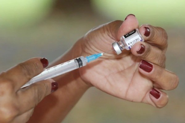 fotografia colorida.  A mulher dosa a quantidade de vacina em uma seringa