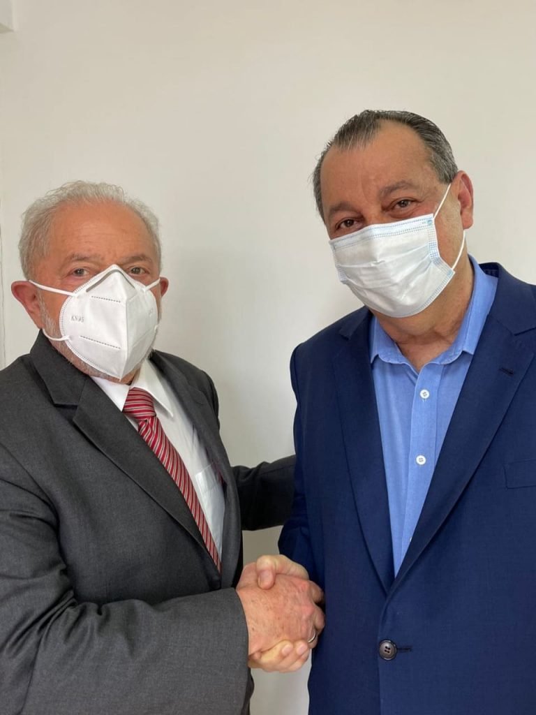 O ex-presidente Lula e o senador Omar Aziz (PSD-AM) se encontraram em São Paulo.  Eles om as mãos, ambos de terno e de máscara, olhando para a câmera - Metrópoles