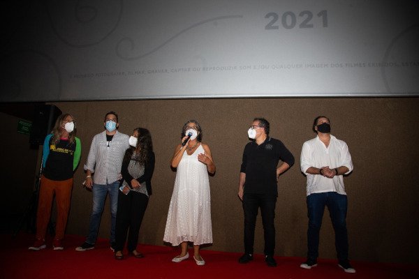 seis pessoas em palco, uma delas segura um microfone