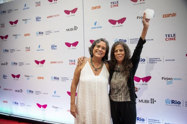 duas mulheres posam, uma delas aponta para cima