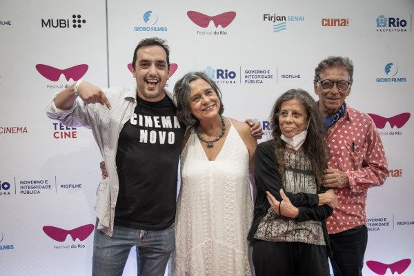 quatro pessoas posam para foto, homem aponta para camiseta onde está escrito 'cinema novo'