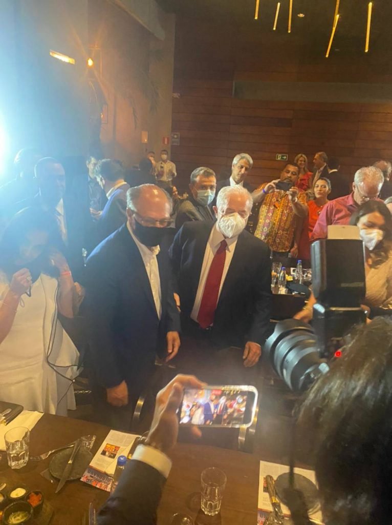 Em jantar possível, Alckmin e Lula se reúnem com aliados e entusiastas de uma aliança.  Eles tiram foto no restaurante cheio, Acompanhados por suas esposas.  Ambos usam terno e conversam - Metrópoles