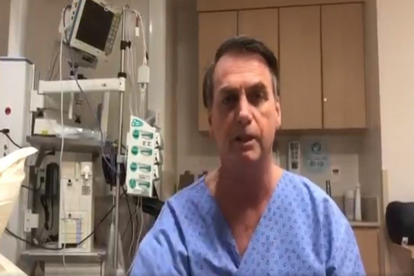 Na imagem colorida, um homem está posicionado no centro. Ele usa roupa de hospital na cor azul e olha seriamente para a camera