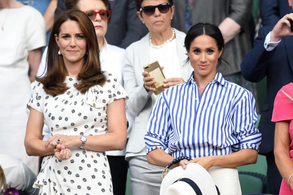 Fotografia colorida. Kate e Meghan posam lado a lado em pé em arquibancada