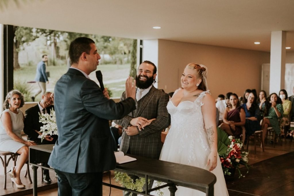 Pastel com caldo de cana: casal comemora união em pastelaria no DF - Veja fotos 5 Casal postado em frente ao juiz de paz na celebração do casamento, com convidados ao fundo