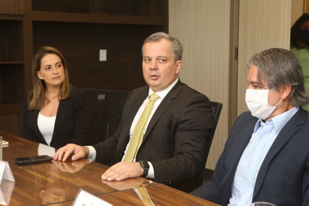 Mulher e dois homens de terno sentados à mesa