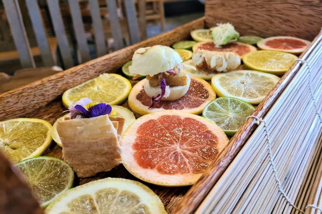 na foto temos uma base de madeira com fatias de laranja e outras frutas critricas e por cima pequenos petiscos